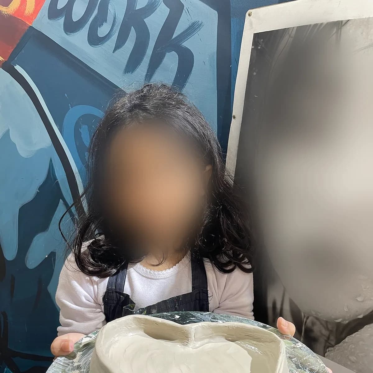 A child proudly holding a heart-shaped clay dish – kids pottery class, arts plastiques workshop