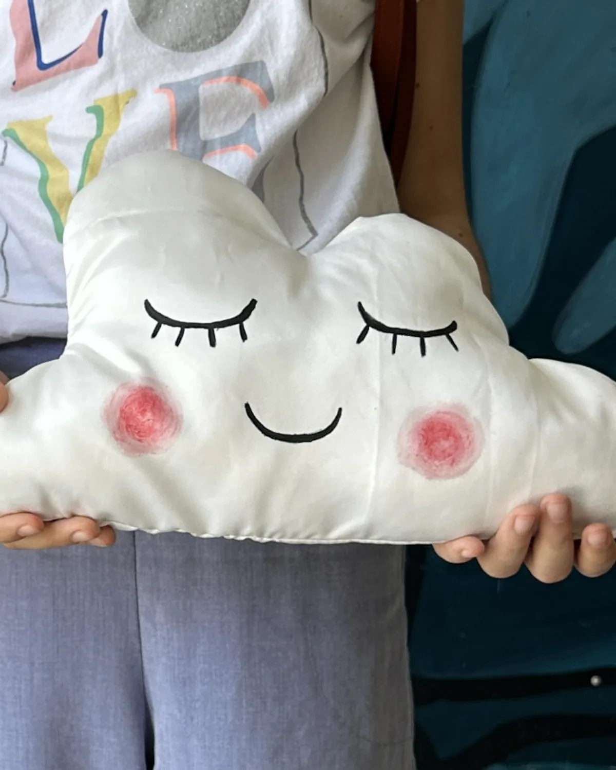 A handmade cloud pillow with a hand-painted face, made in a Bluhimi Arts DIY workshop