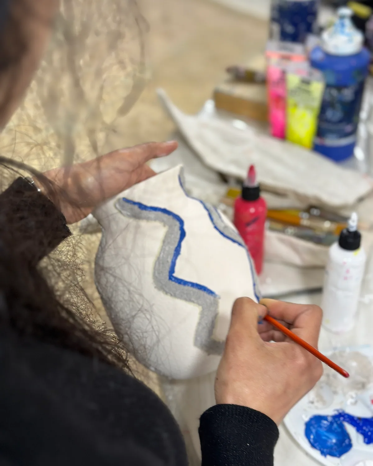 Hands painting a blue wave pattern on a white ceramic piece – ceramic painting, an arts plastiques workshop in Casablanca & Fès