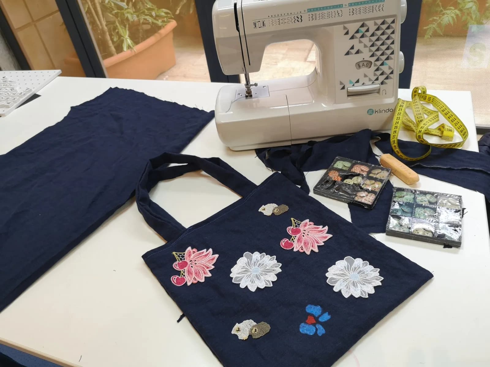A navy tote bag decorated with embroidered flowers beside a sewing machine – sewing and creative arts plastiques workshop