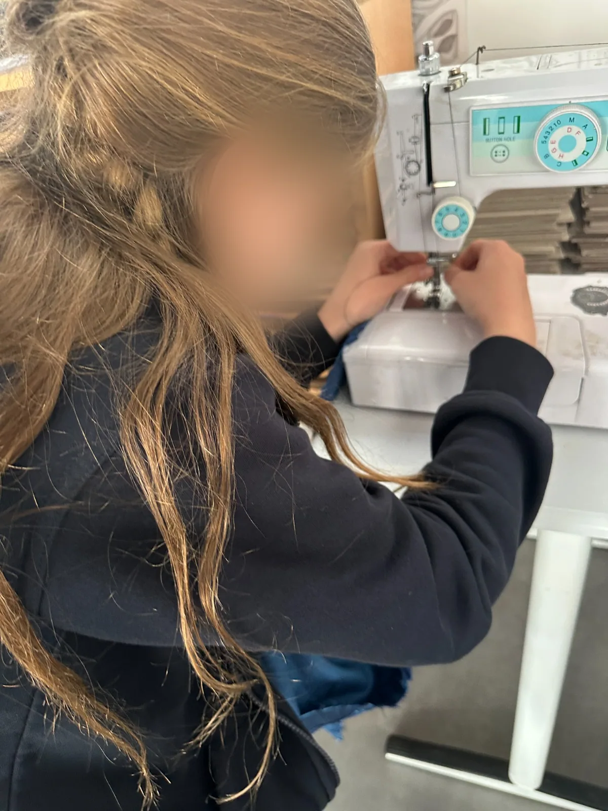 A girl guiding fabric through a sewing machine – sewing workshop, part of our arts plastiques creative workshops