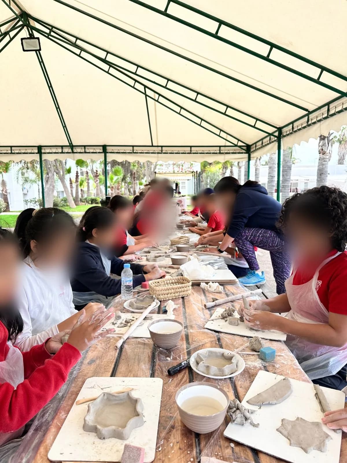 Children hand-building clay dishes along a long table under a garden tent – kids pottery and arts plastiques workshop