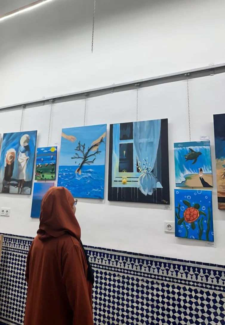 A visitor looking at paintings hanging on an exhibition wall at Bluhimi Arts – arts plastiques exhibition
