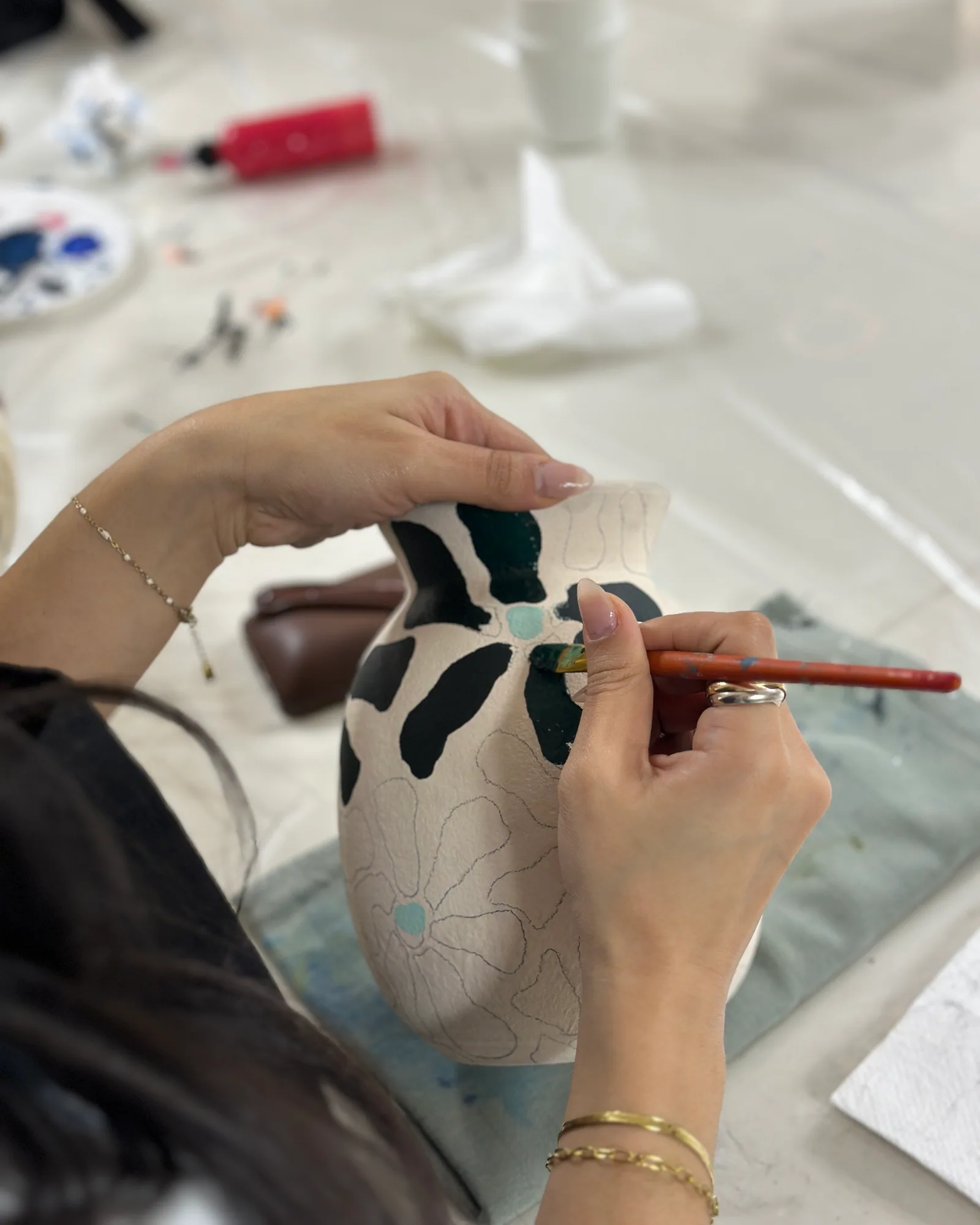 Hands painting a floral pattern on a ceramic vase – arts plastiques workshop at Bluhimi Arts