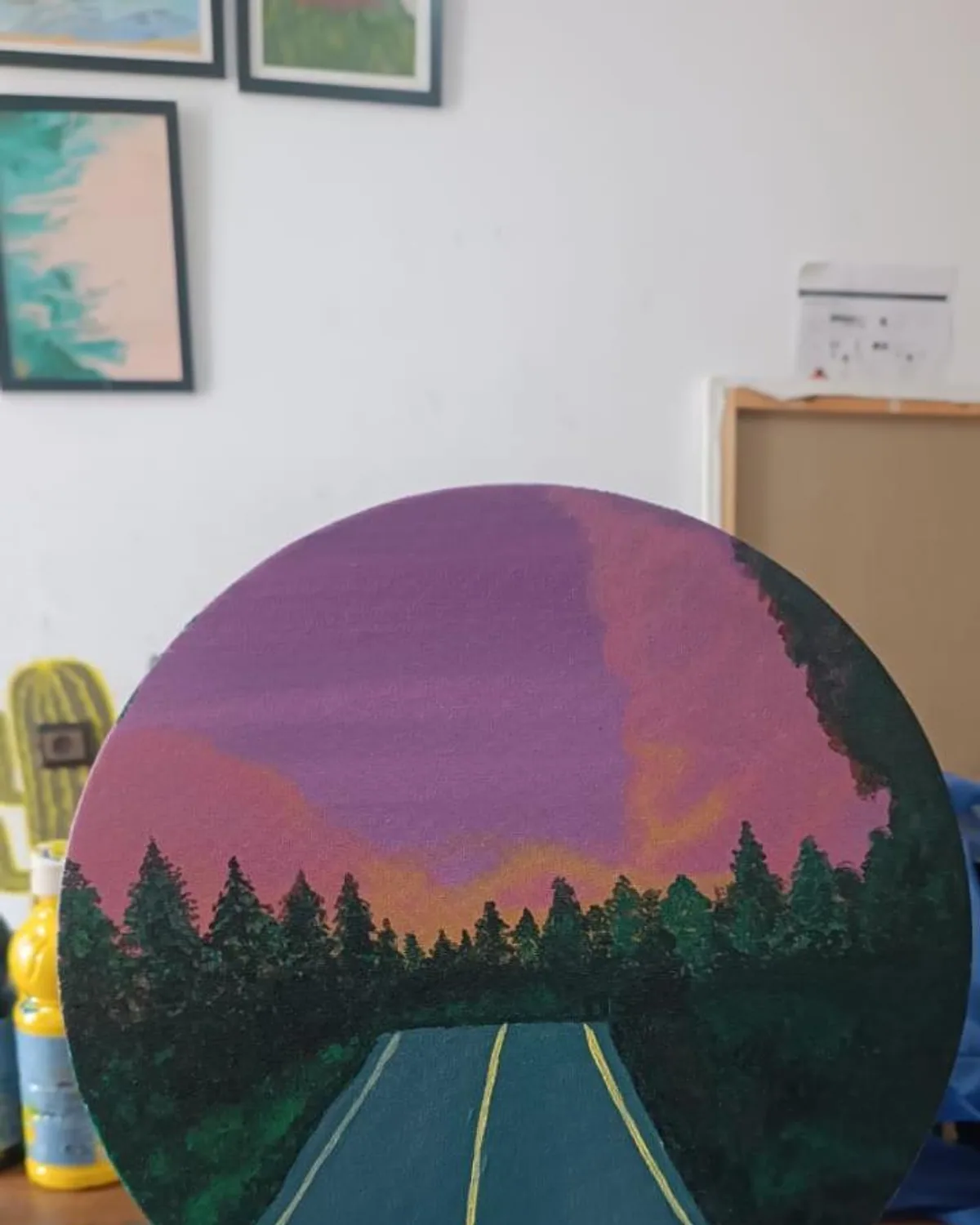 A circular painting of a sunset over a forest road