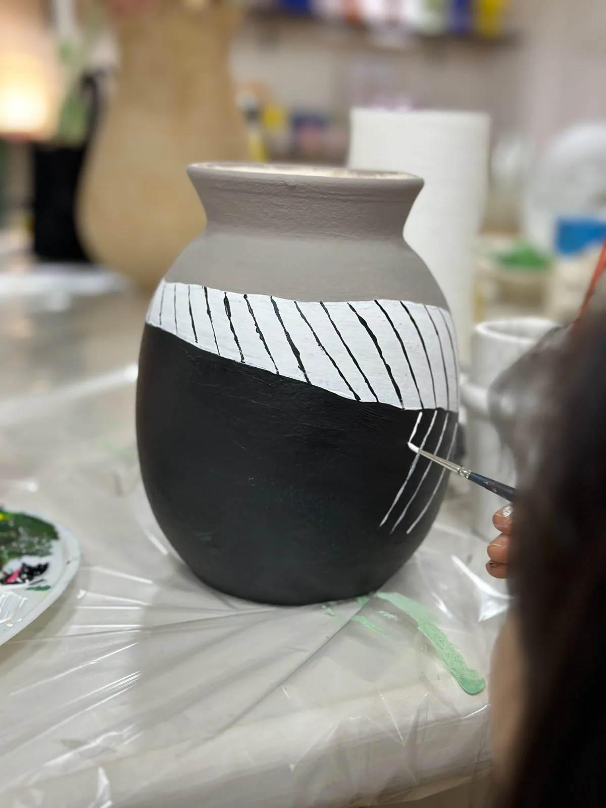 A vase with a black body being hand-painted with white stripes
