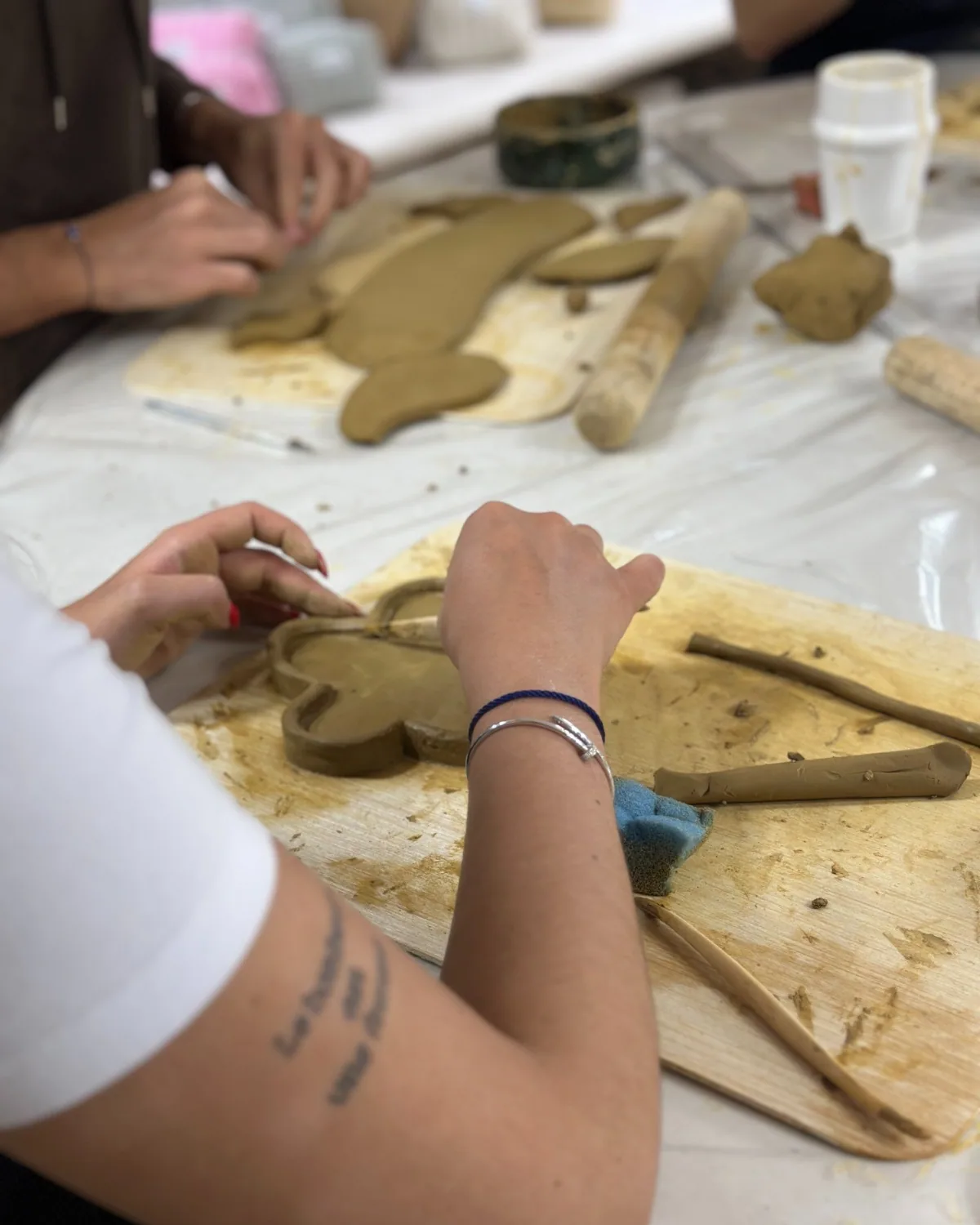 Hands shaping a clay dish on a wooden board – pottery class, arts plastiques workshop in Casablanca & Fès